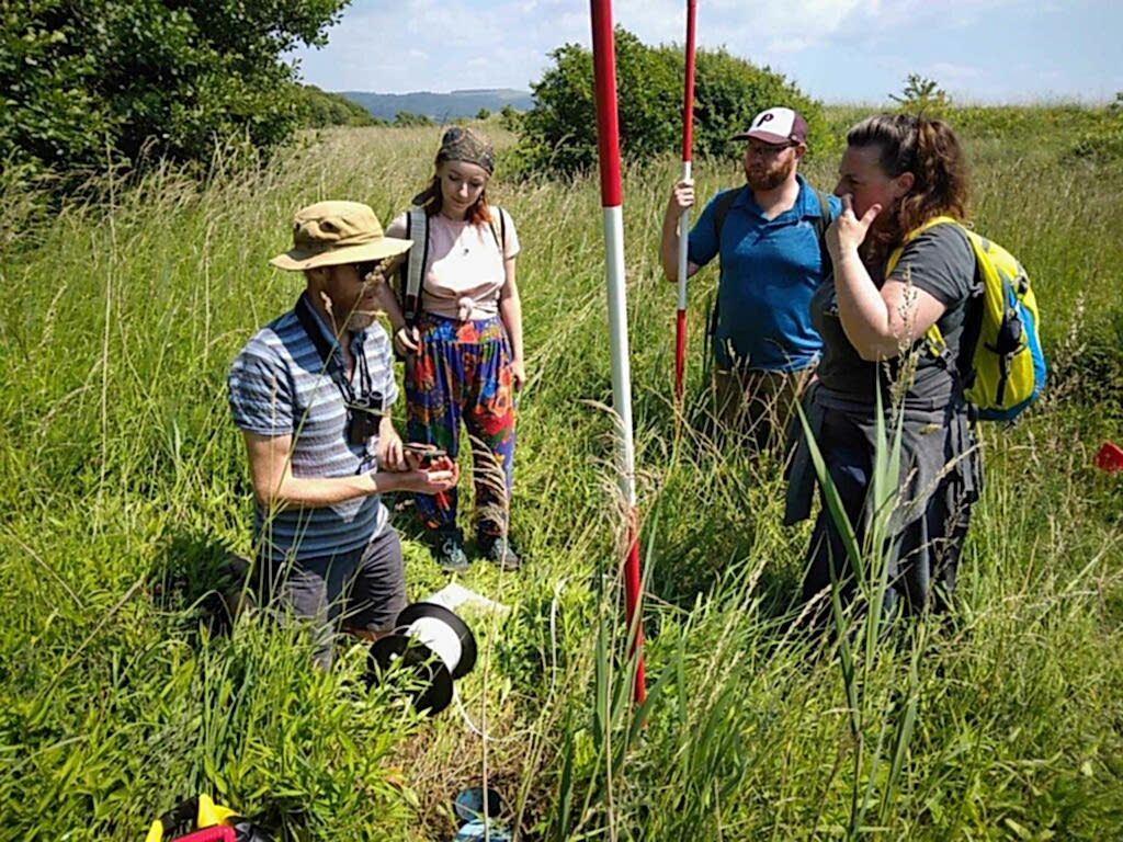 A group of people gather outdoors to talk about how to survey a sand dune.