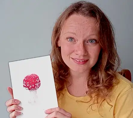 Woman holding watercolour painting of a Fly Agaric mushroom