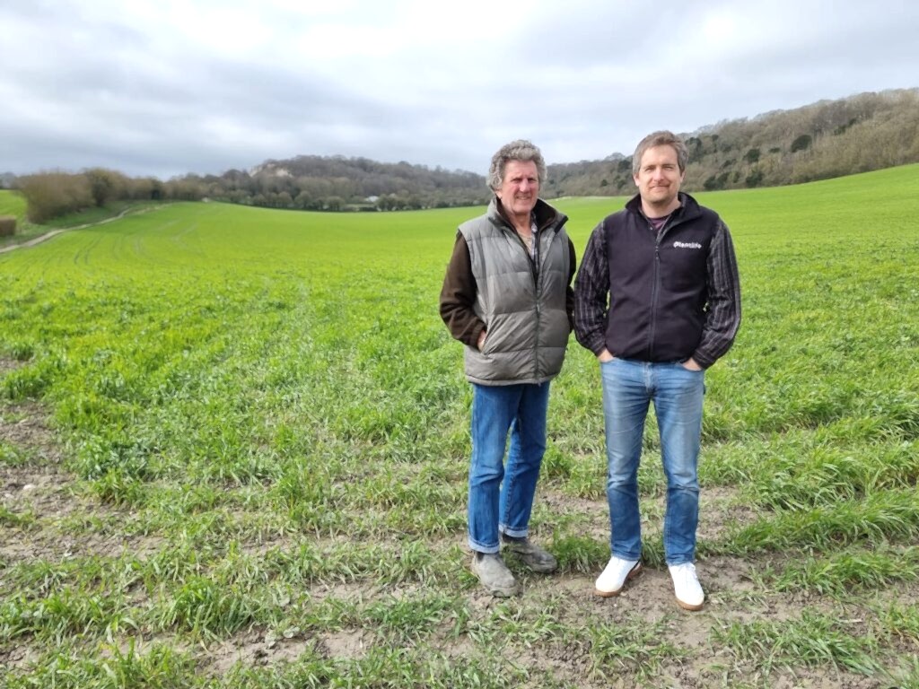 Two men stood together in front of a field on a farm