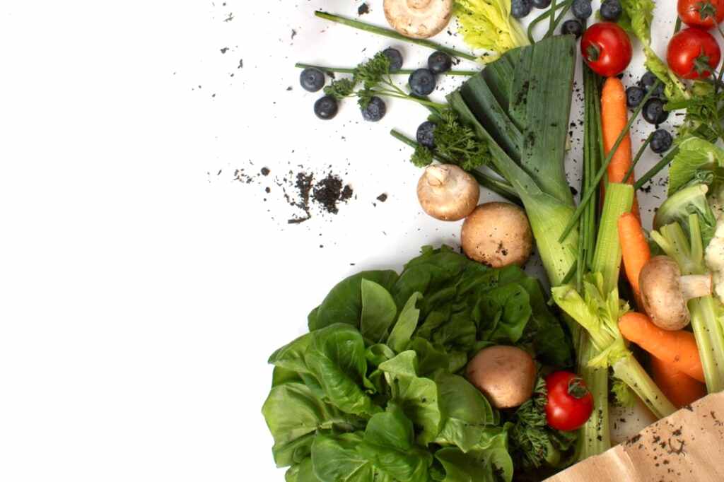 Photograph shows vegetables spilling out on to a white table from a brown paper bag. Over the vegetables and on to the white surface are bits of peat - showing that peat was used in the growing process for all of these every day vegetables.